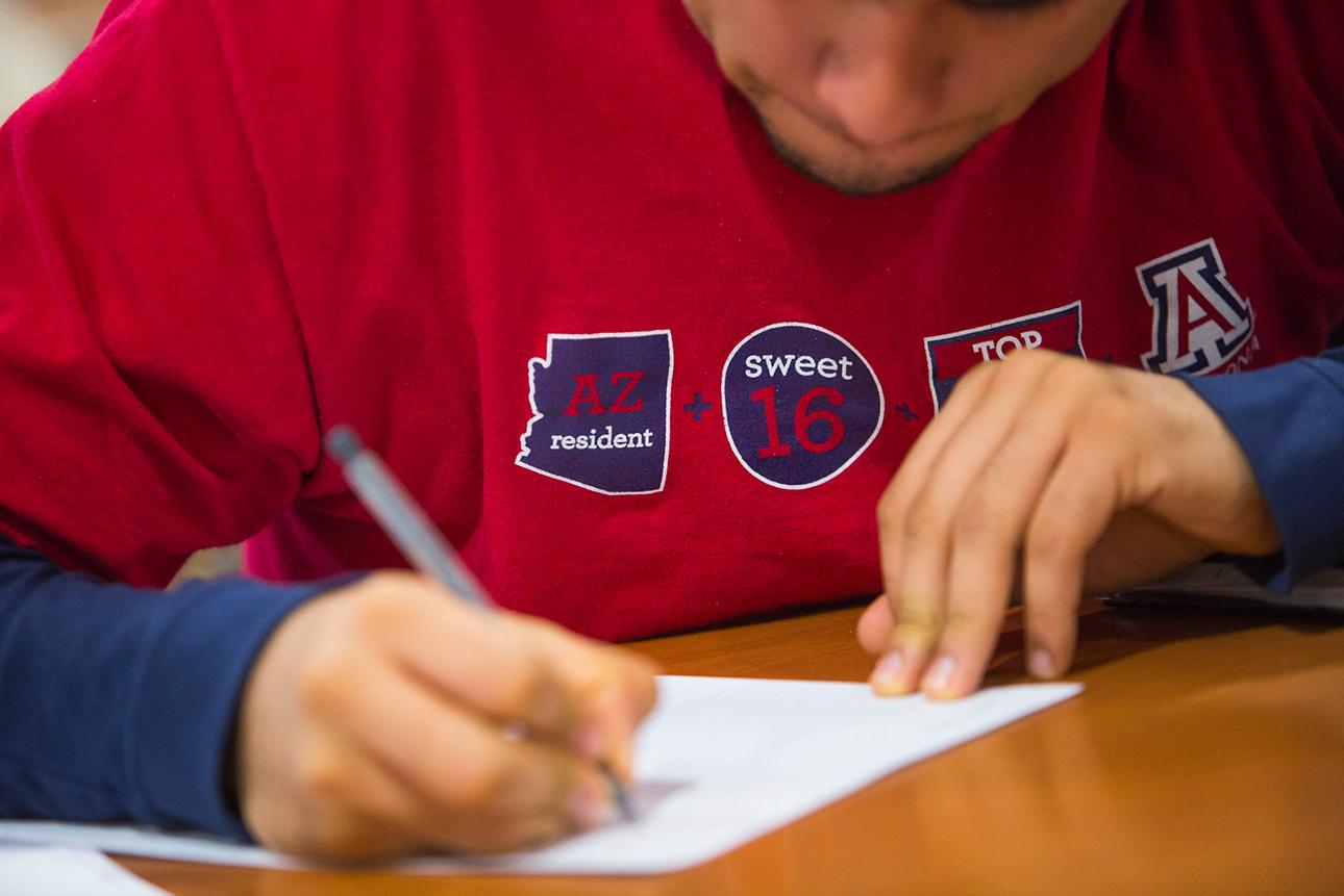 Male student wearing red UA shirt writing at desk
